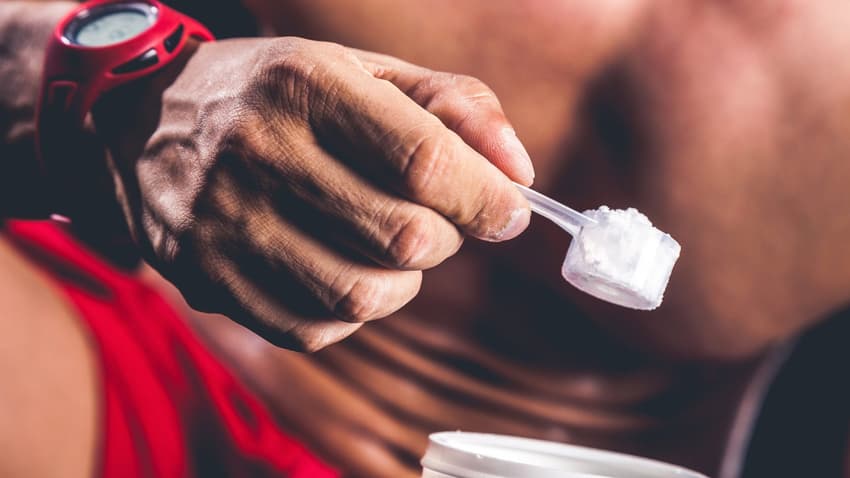 homem prestes a treinar sem camisa com close em seu abdomen e mãos segurando um scoop de creatina